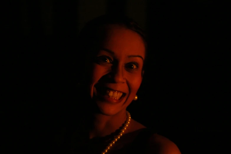 the woman is smiling in the dark wearing a pearl necklace