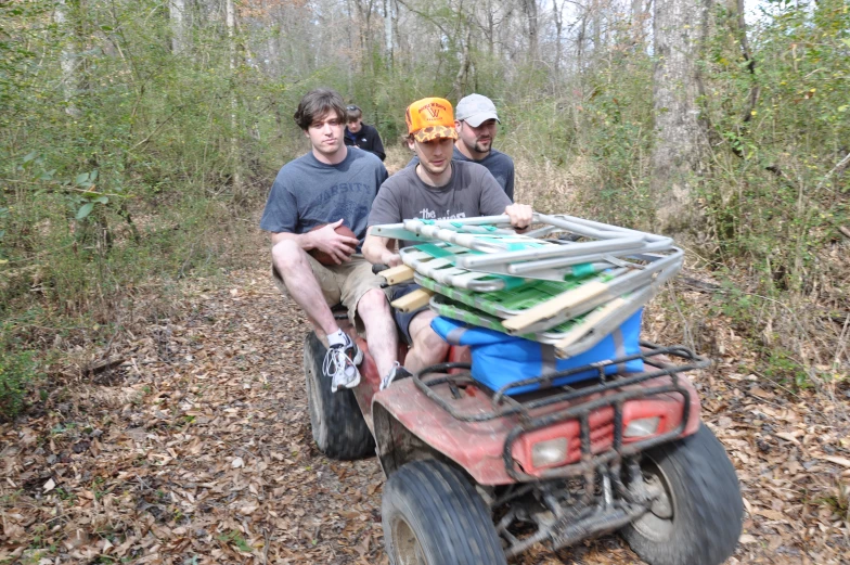 a group of men ride on four wheelers in the woods