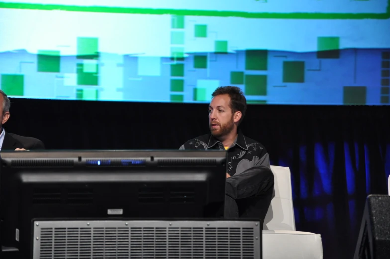 two men at a panel in front of large screen tv