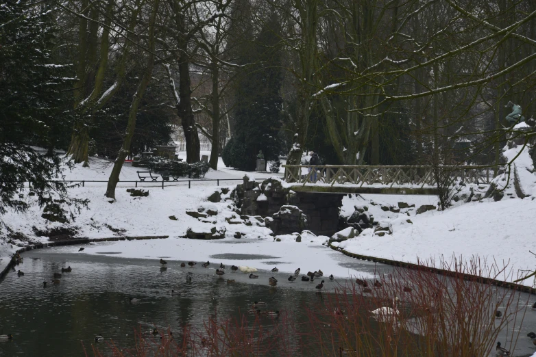 a winter scene with a stream, snow and bridge