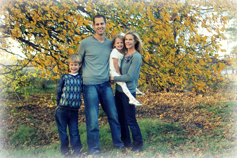 a family poses in front of a tree for an outdoor portrait