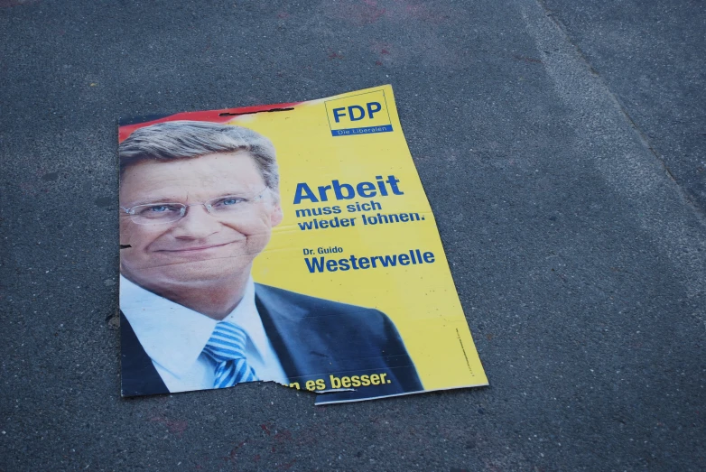 a newspaper with the image of a man wearing glasses and a tie is lying on pavement