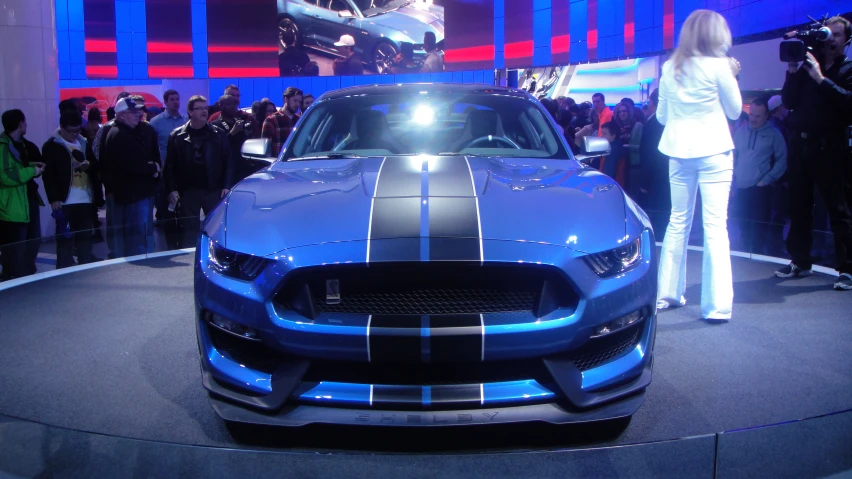 a woman in white stands near a blue sports car