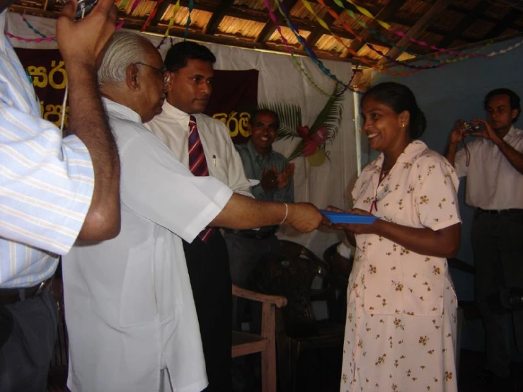 two men shake hands with some people standing around