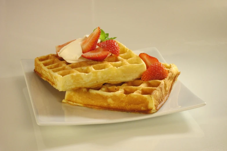 three waffles sitting on top of each other with strawberries and whipped cream on top