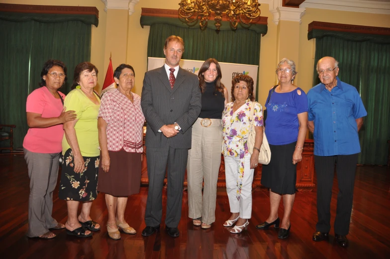 an older man poses with six women and two men in front of him