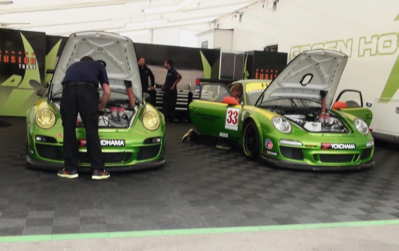 two green cars on display in a showroom with one man and the other woman looking at them