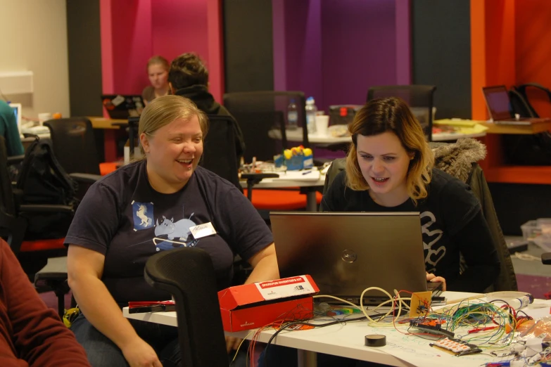 two women are at a desk working on a laptop computer