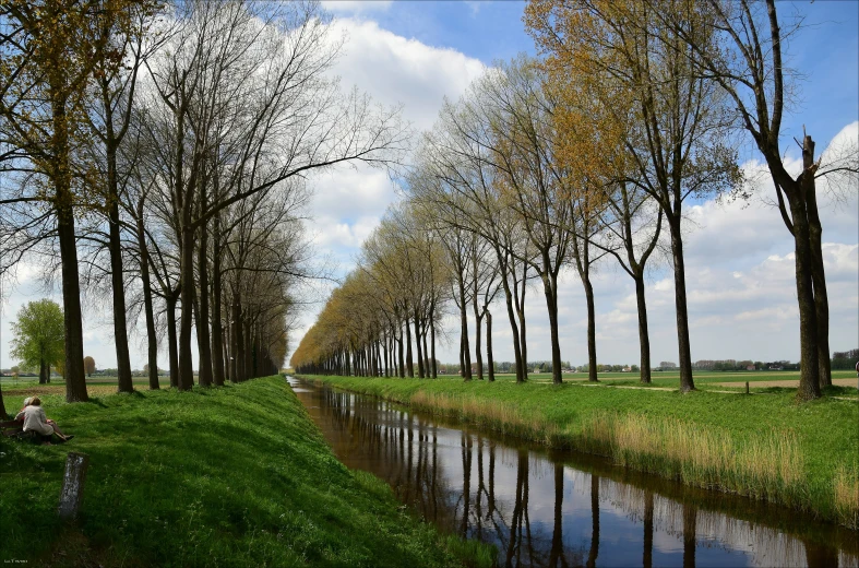 there is a man sitting on the bank of a canal