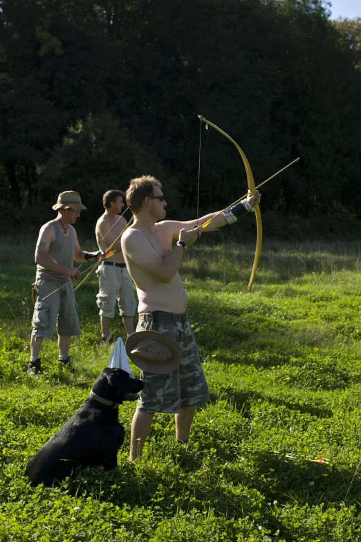 three men are in a grassy area with a black dog