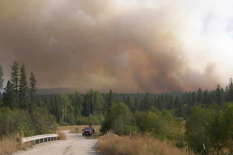 a large cloud of smoke in the distance and cars on a road in front