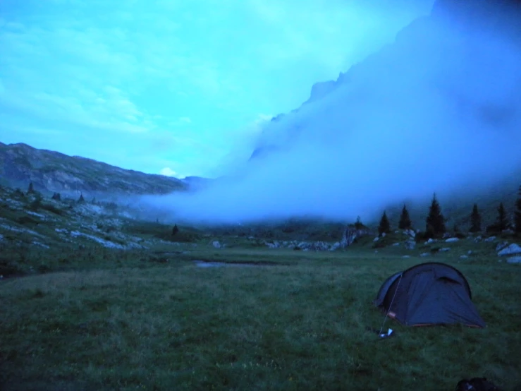 a tent is pitched up in a field with mountains in the distance