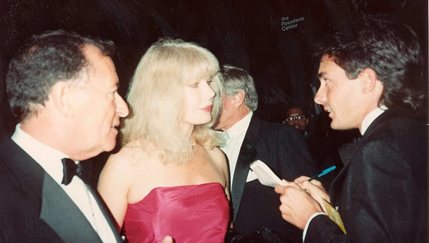 a woman in red dress standing next to a man in a black suit