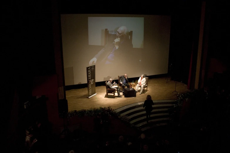 the people are sitting on a stage in a darkened place