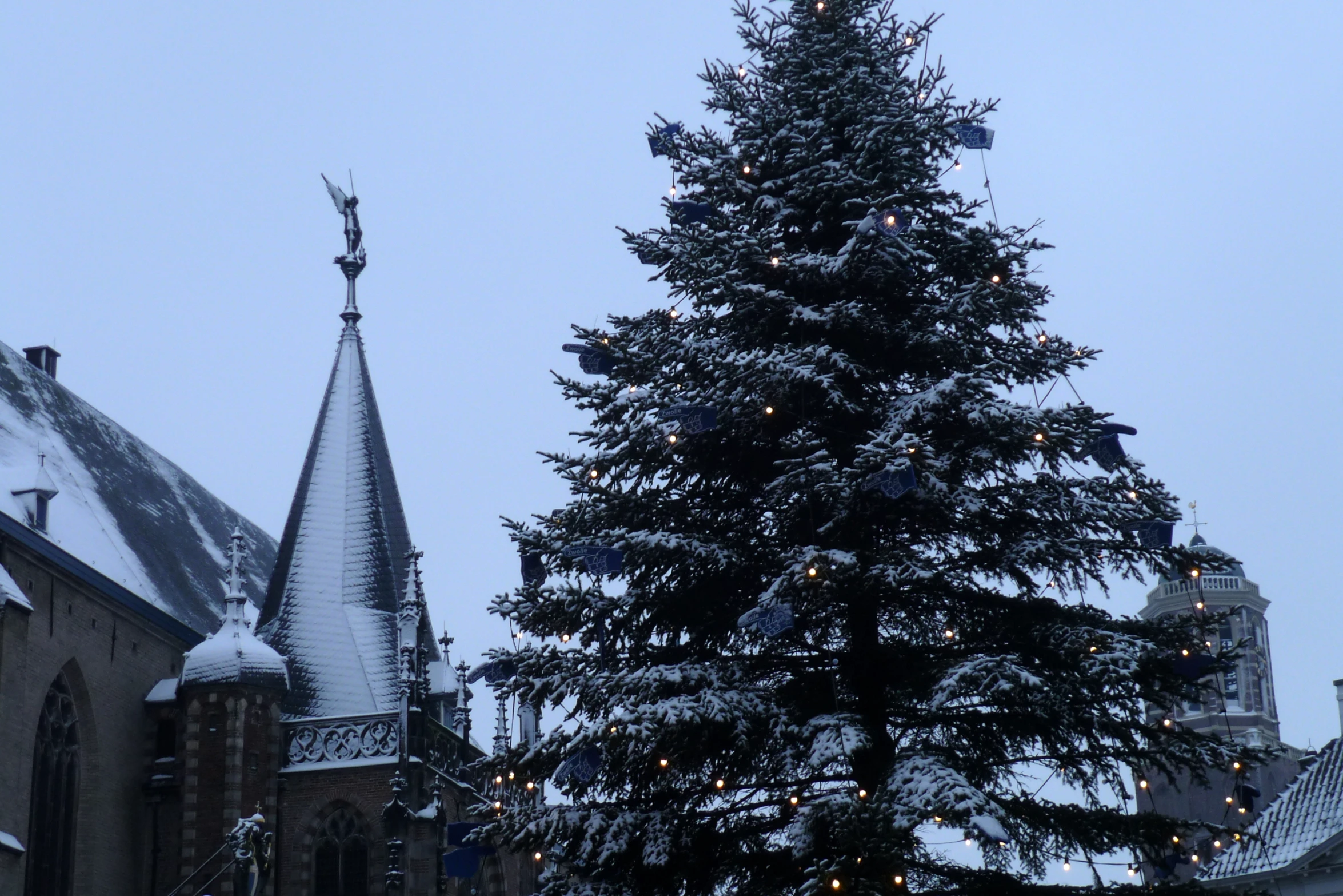 a large christmas tree in front of a building with lights and a steeple