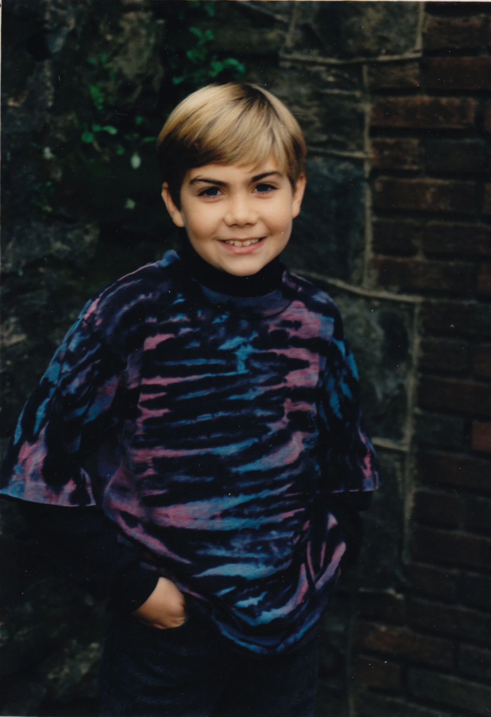 a boy wearing a tie dyed shirt and standing by a wall