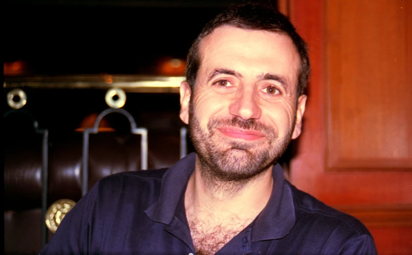 a man wearing a dark colored shirt smiles at the camera