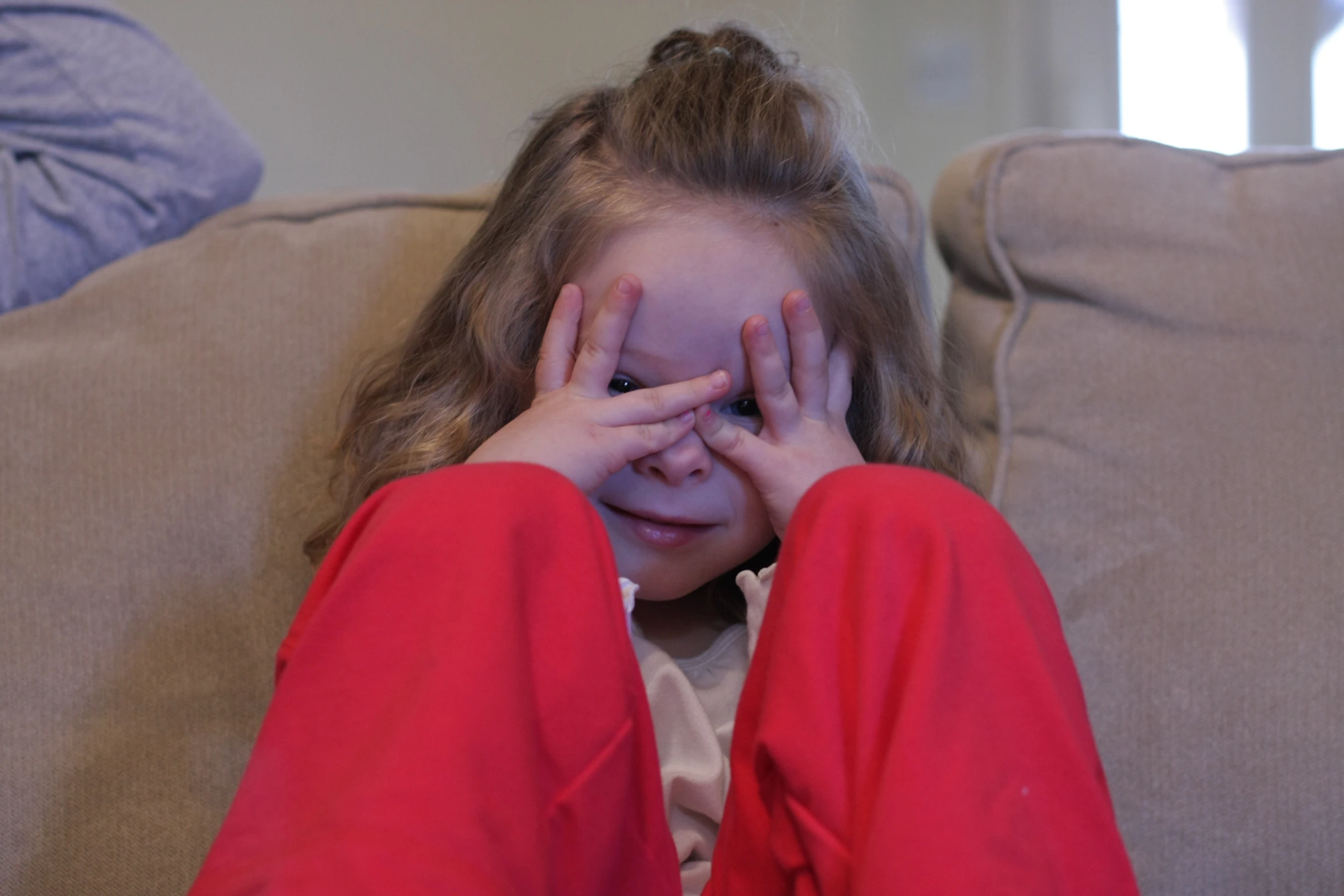 a little girl sitting on a couch covering her face with her hands