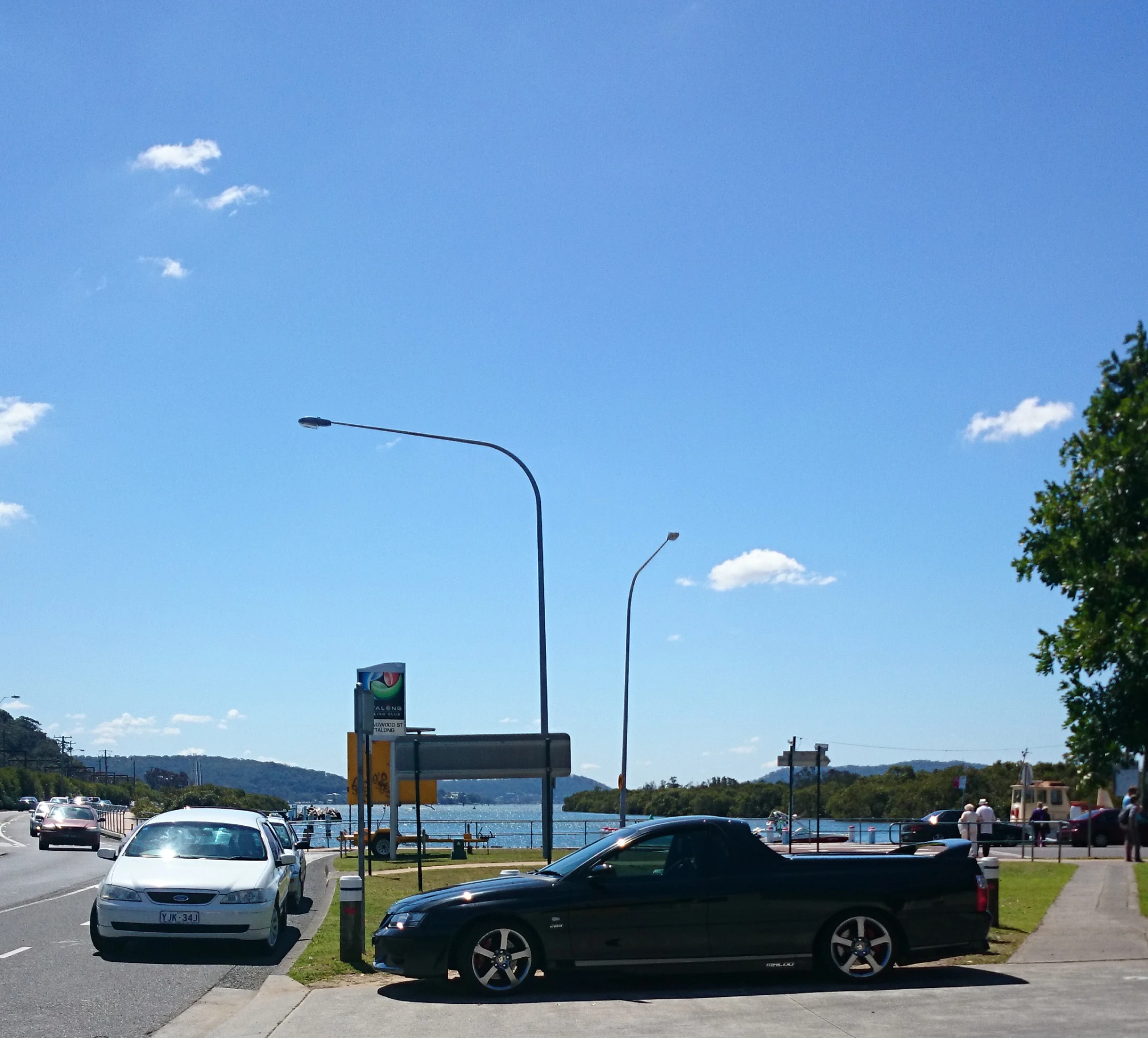 two cars stopped at the side of a road next to water