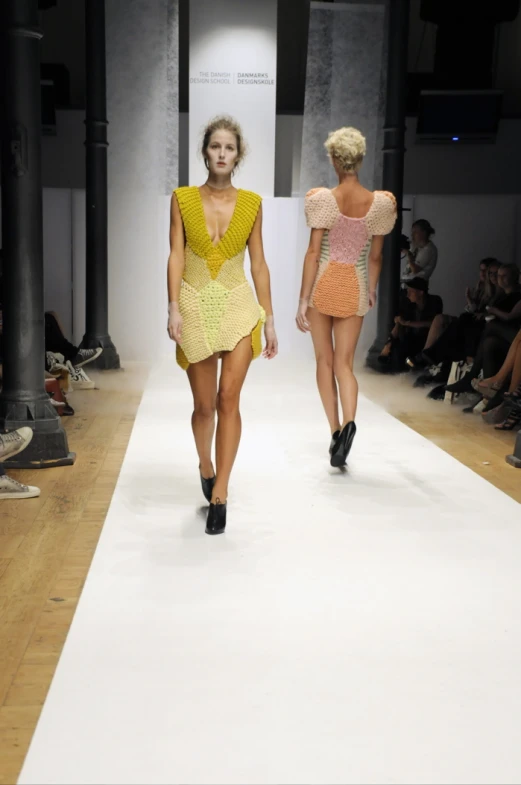 two woman walking down a runway, in high heels