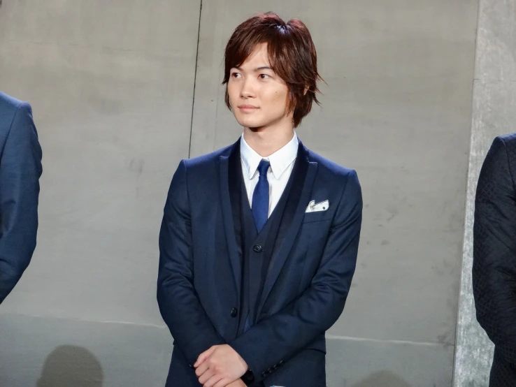 young man in blue suit and tie standing with two other people