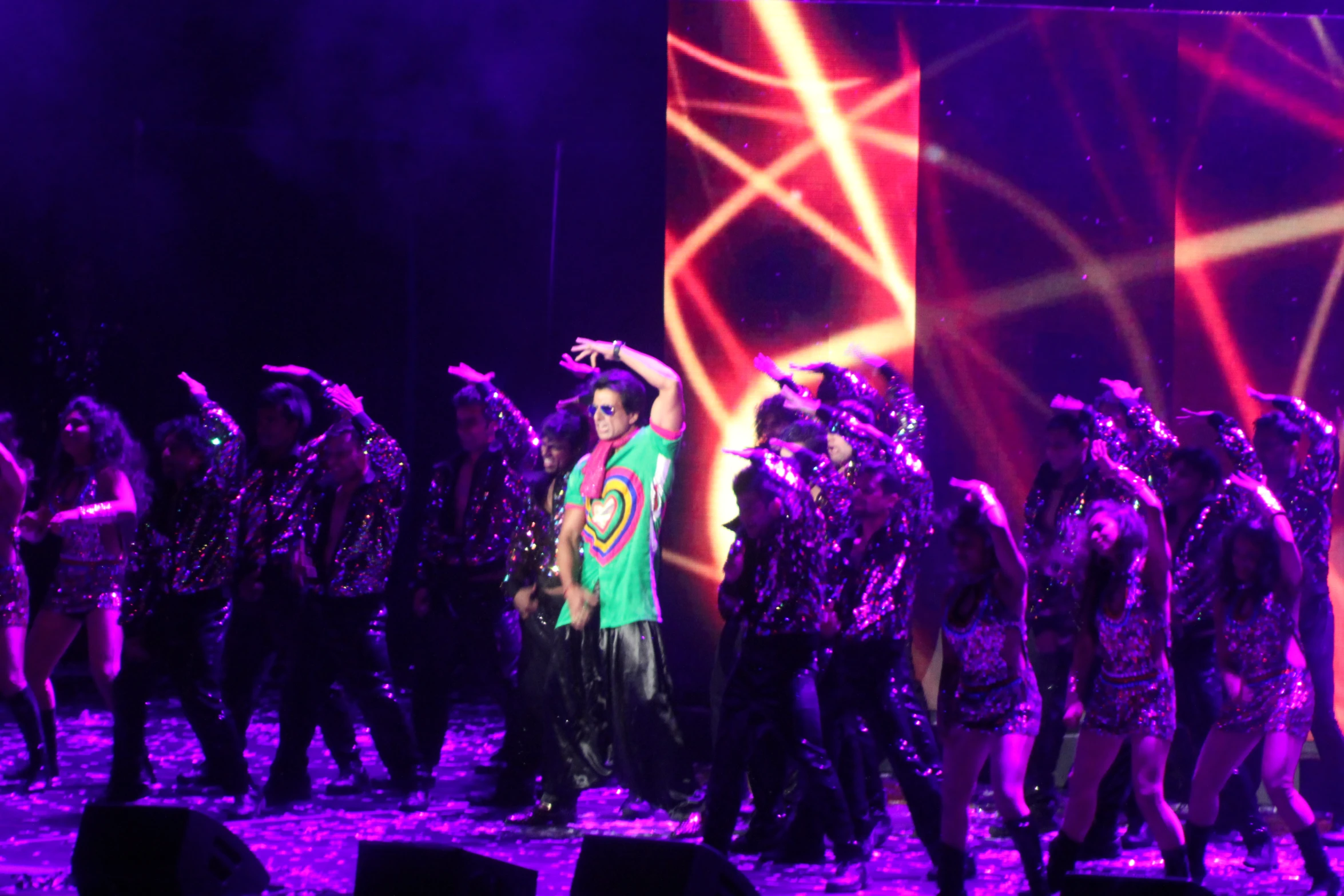 a man in purple stands on stage with his hands up