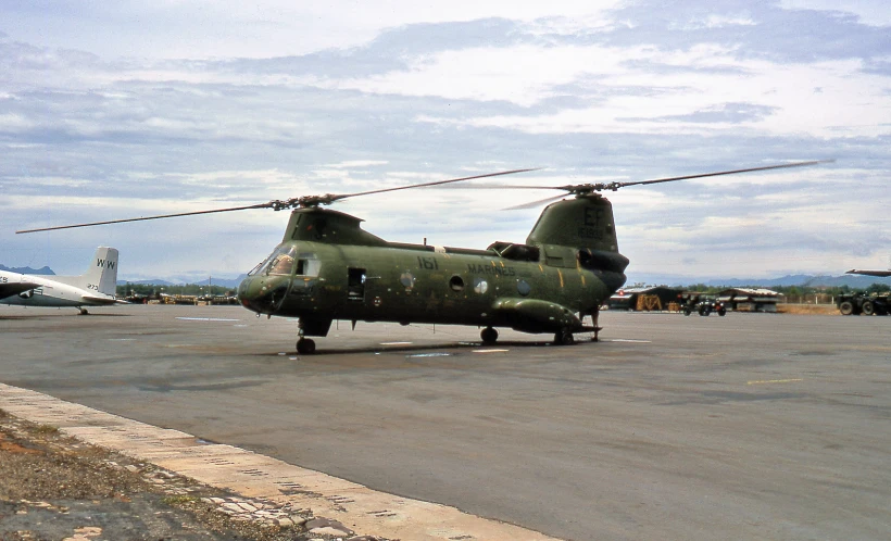 an army green helicopter sits on the runway