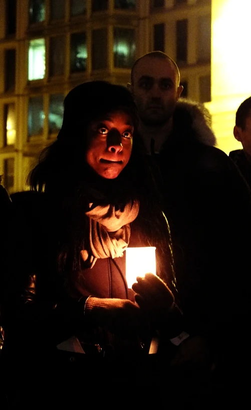 a girl holding a lit candle looks at the camera