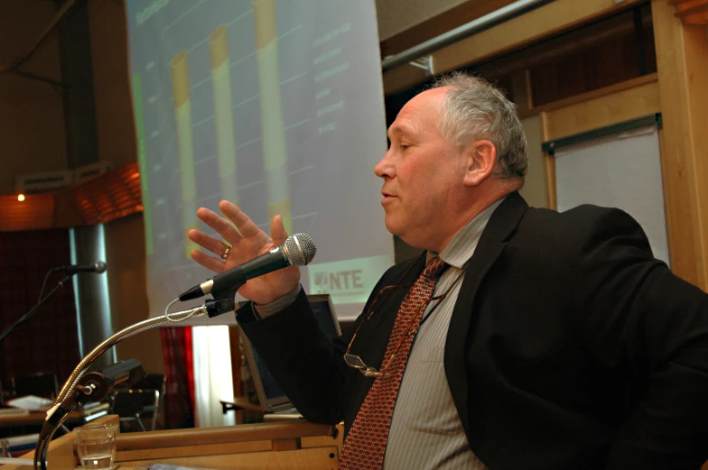 a man speaking in front of a large screen