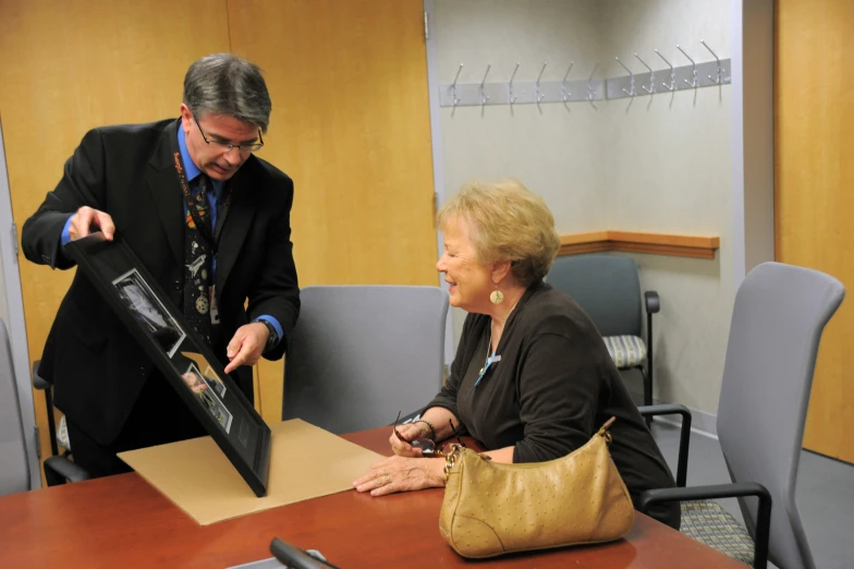 an elderly woman receiving a greeting card from a man in an office