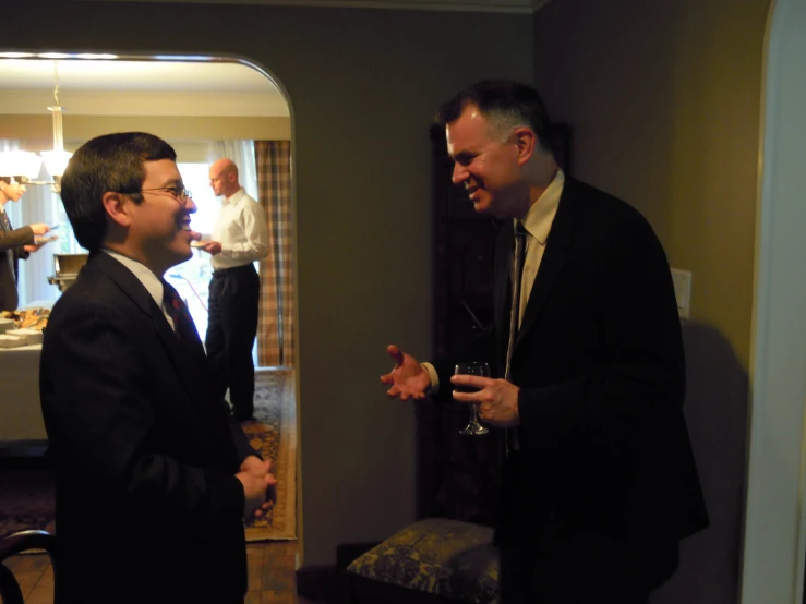 two men in suits, one talking to the other holding glasses