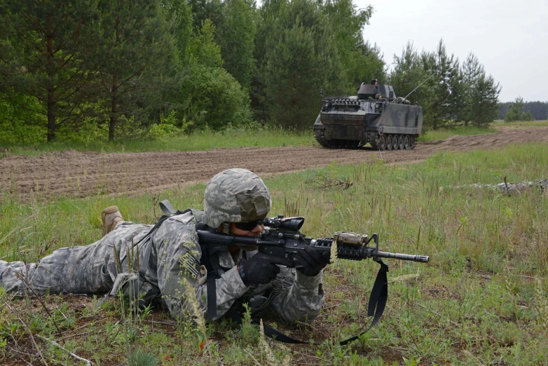 a soldier laying in the grass next to a tank