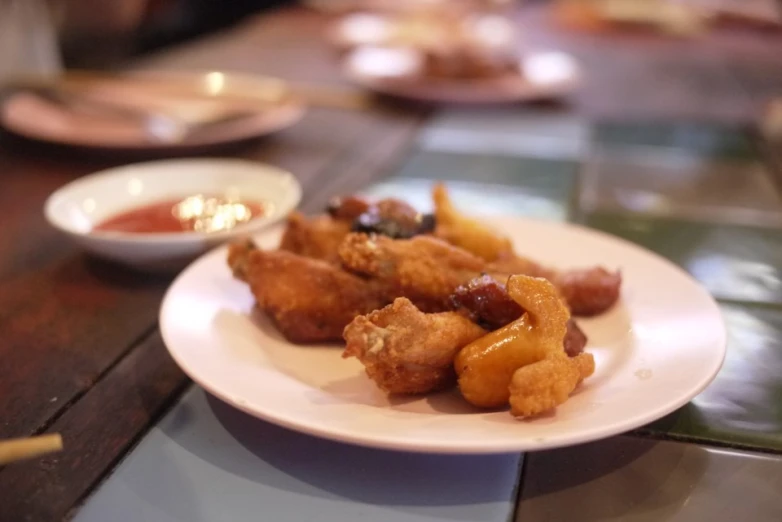 a plate with fried food, sitting on a table next to a bowl of dipping sauce