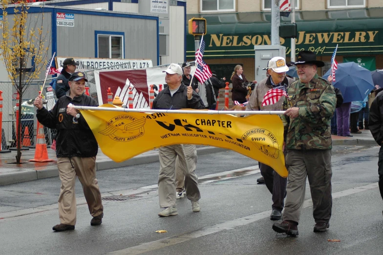 a parade has men holding flags, a banner and some umbrellas