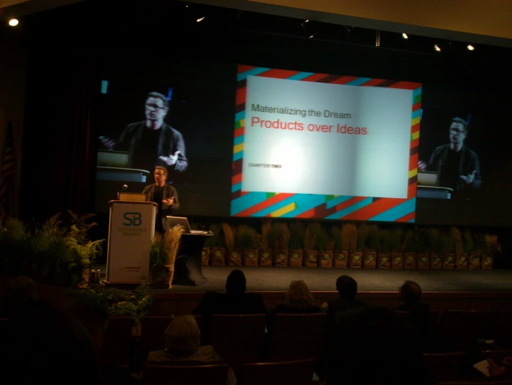 man standing on stage speaking at conference in front of audience