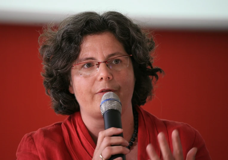 a woman standing with her hands out in front of her face and speaking into a microphone