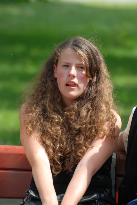 a girl sitting on a bench with a long curly hair