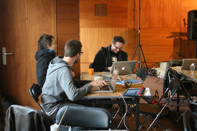 three men sitting at table with laptop computers