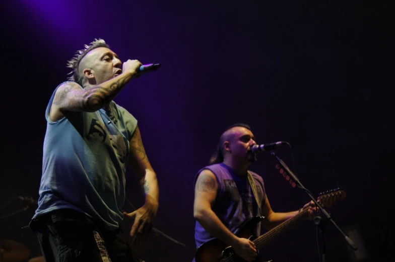 two guys are on stage singing while holding their guitars