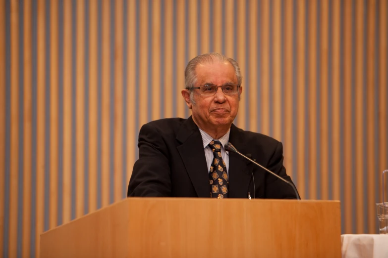 a man in a suit sitting at a table with a microphone