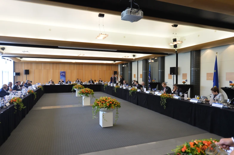 several people seated at long black tables with many plants