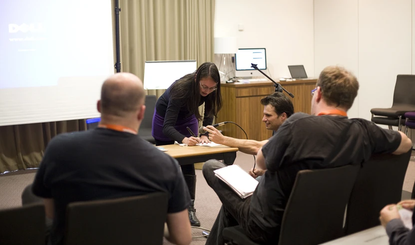 a woman signing papers for people who are sitting at desks