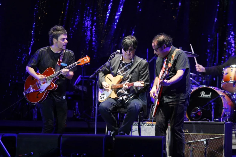 three people are playing guitars on stage together