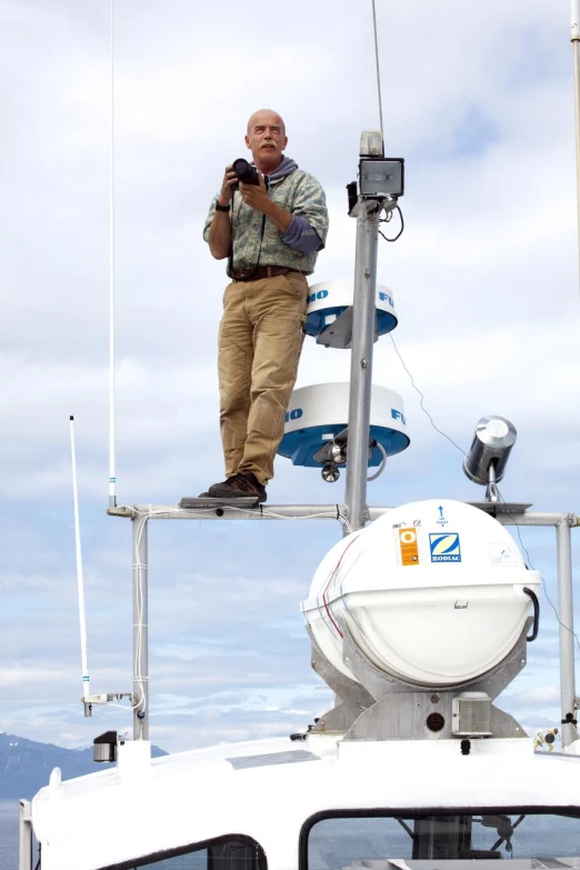 man standing on boat mast and holding camera