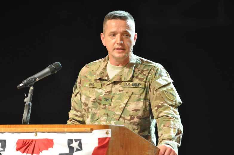 a man in camouflage stands at a podium in front of a microphone