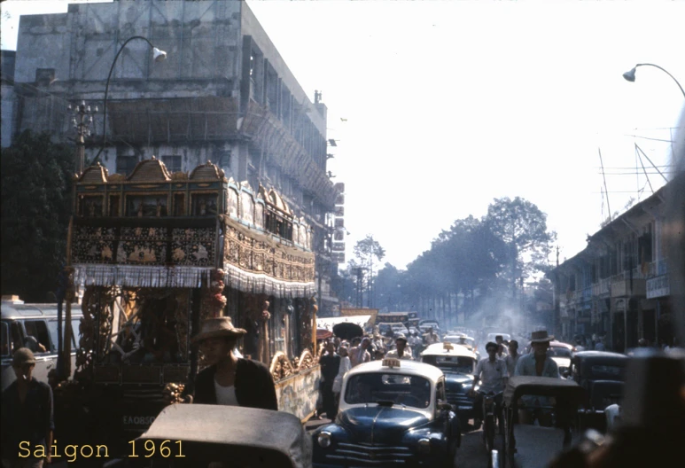 an old - fashioned car with many people riding through a crowded city street