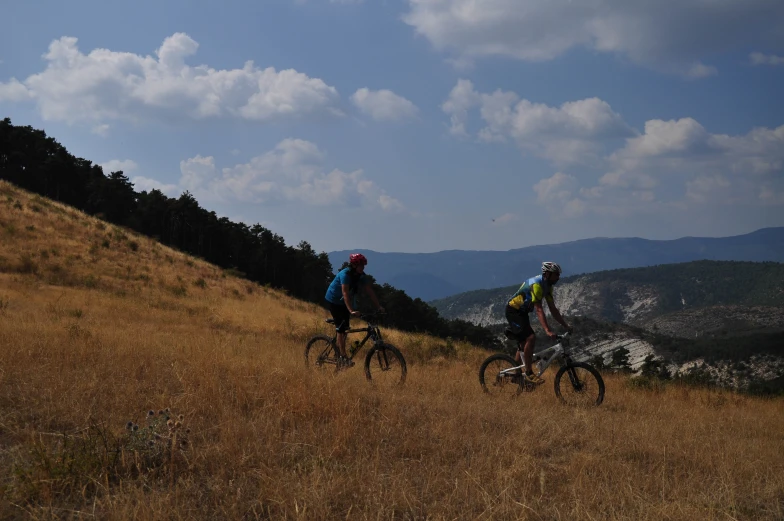 two people wearing helmets riding bicycles on the side of a hill