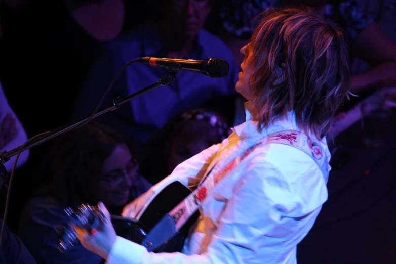 the man with the long hair holds up a guitar while singing