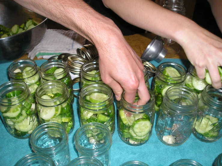 a person is assembling cucumbers in mason jars on a table