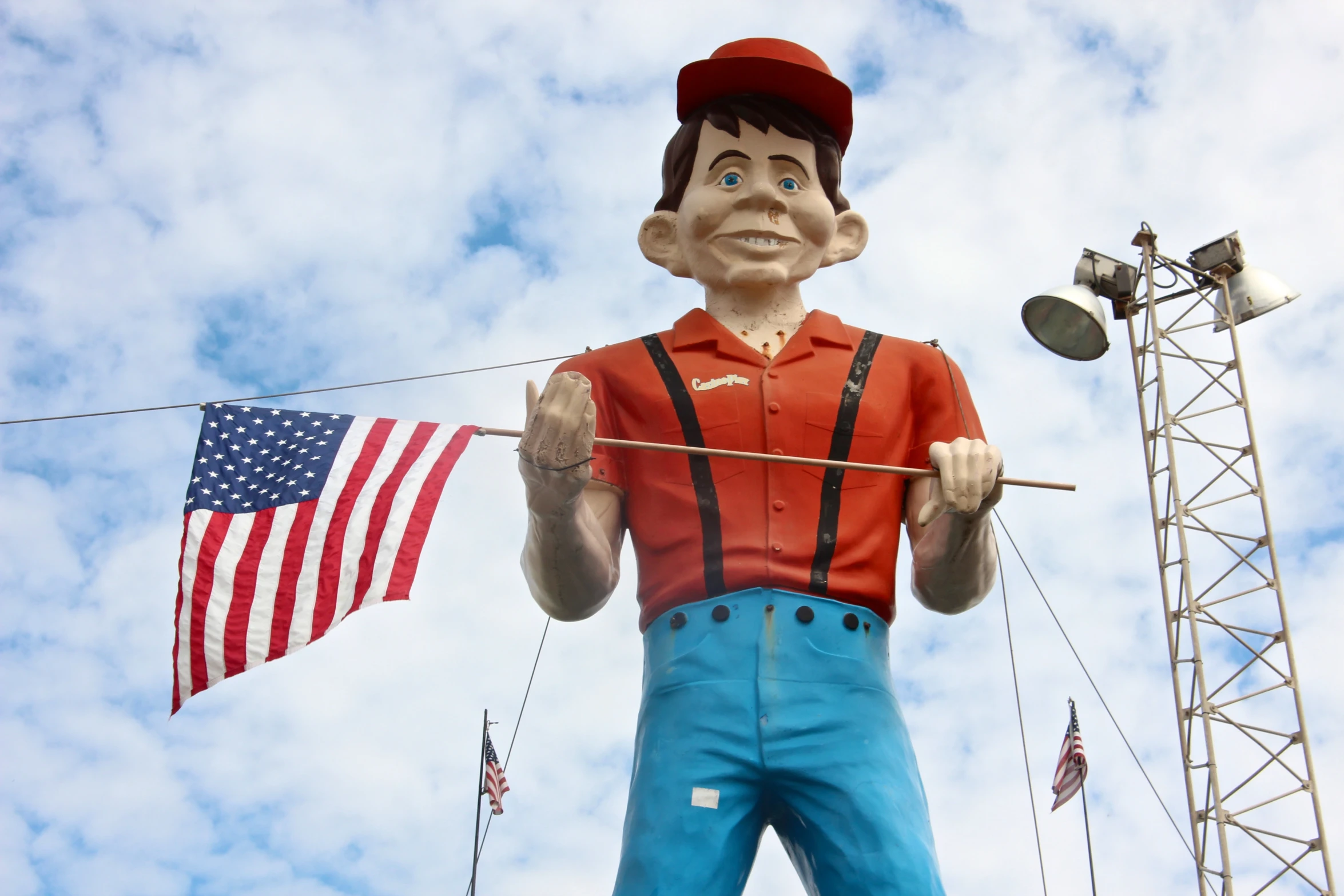 a statue of a worker in overalls standing next to a tall mast